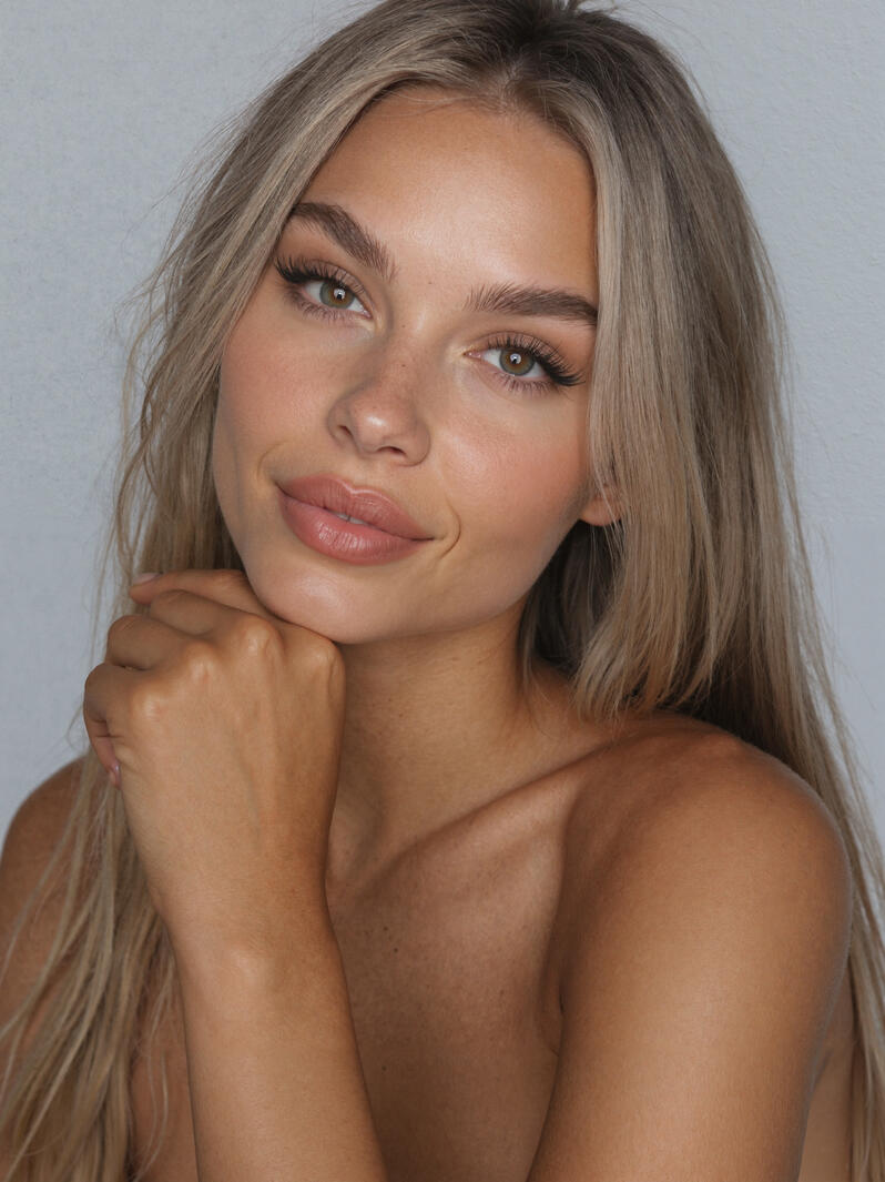 Close-up portrait of Mia Liorvain with hand under chin against a gray studio backdrop.